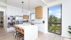 A modern kitchen with white cabinetry, stainless steel appliances, and a large island with bar stools. - SeaDreams 5: Oceanfront Condos w/Pool, Hot Tub, & Rooftop Patio (West Bay)
