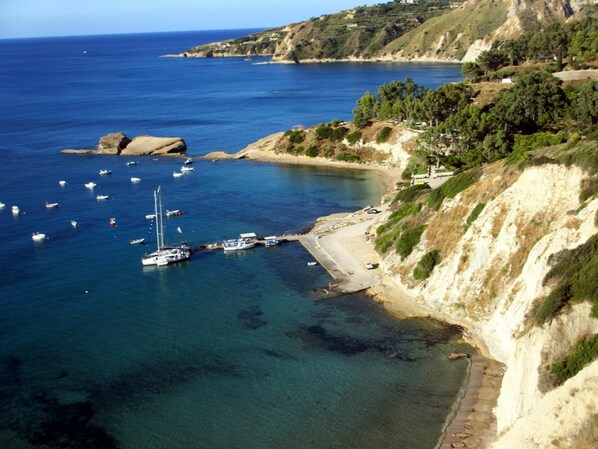 A coastal area with boats docked at a pier, a sandy beach, and a rocky cliff with vegetation.