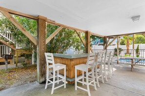 An outdoor bar area with a wooden structure, white chairs, and a view of a swimming pool and greenery. - 6BR Home with Private Pool and Walk to Beach (Surfside Beach)
