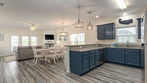Una cucina moderna con mobili blu scuro, un piano di lavoro in granito e una lavastoviglie integrata. C'è una zona pranzo con un tavolo e sedie bianche, e un ventilatore a soffitto.