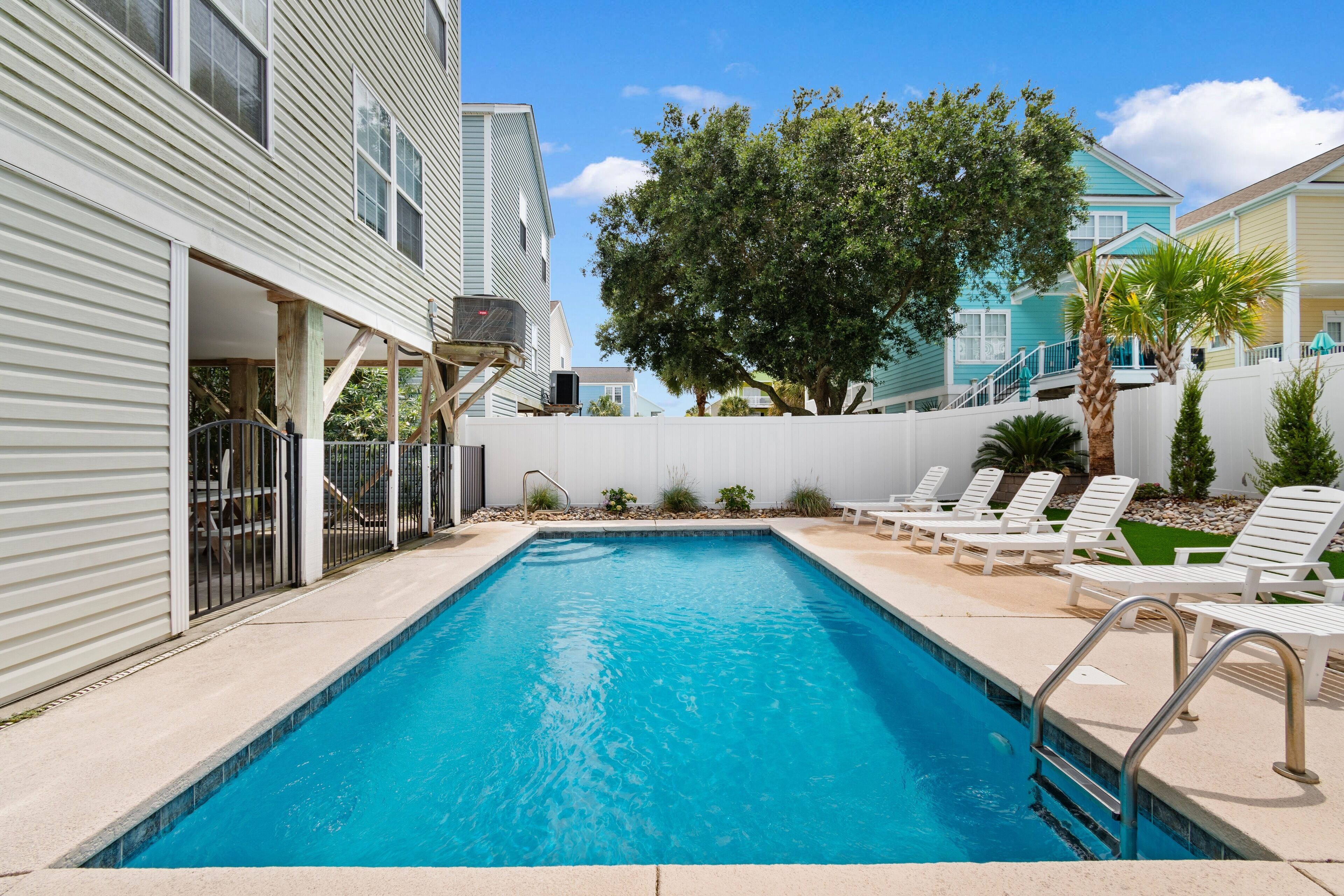 A rectangular swimming pool with a metal ladder on one side, surrounded by a white fence.