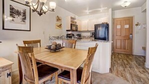 A dining area with a wooden table and chairs, a chandelier, and a kitchen with white cabinets and a refrigerator. - Silver Mill 8167-1br-walk To Slopes! Kids Ski Free! 1 Bedroom Condo by RedAwning (Keystone)