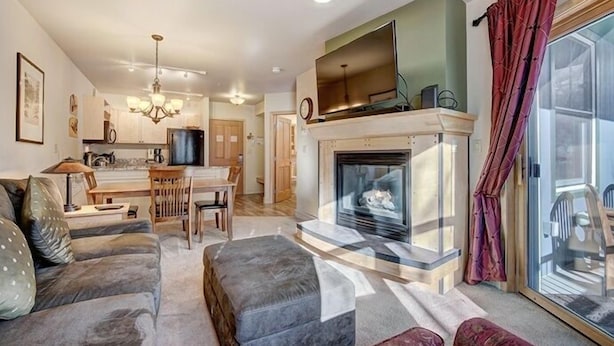 A modern living room with a fireplace, a dining area, and a kitchen in the background. - Silver Mill 8167-1br-walk To Slopes! Kids Ski Free! 1 Bedroom Condo by RedAwning (Keystone)