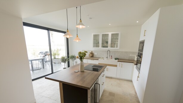 A modern kitchen with a central island, white cabinetry, and a view to an outdoor patio. - Maison Chaleureuse en Bord de Loire (La bohalle)