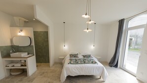 A modern bedroom with a large bed, a built-in bench with a mirror, a small bedside table, and a large window with a view. - Maison Chaleureuse en Bord de Loire (La bohalle)