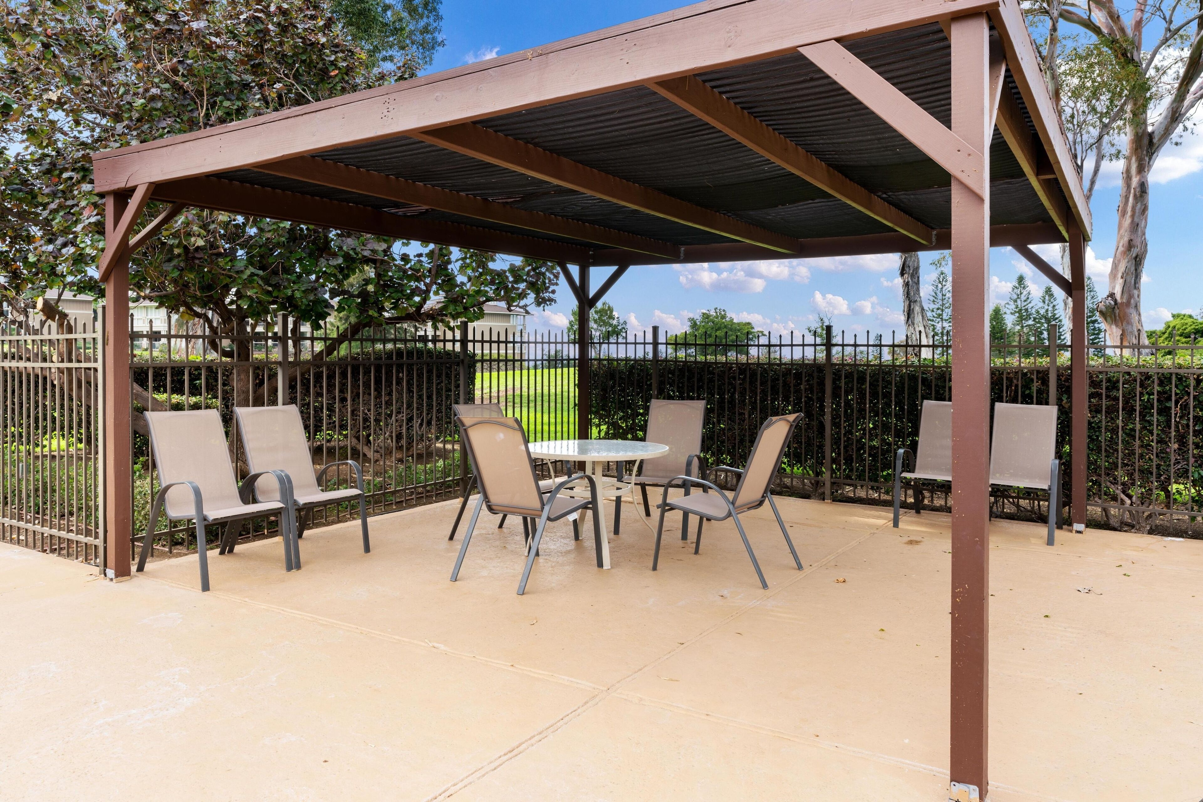 A covered patio area with a table and chairs, surrounded by a metal fence.
