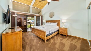 A bedroom with a wooden bed, a ceiling fan, a TV, and a view of the outside.