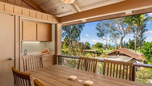 A wooden dining table with chairs, a kitchen area with cabinets, and a view of a golf course and palm trees.