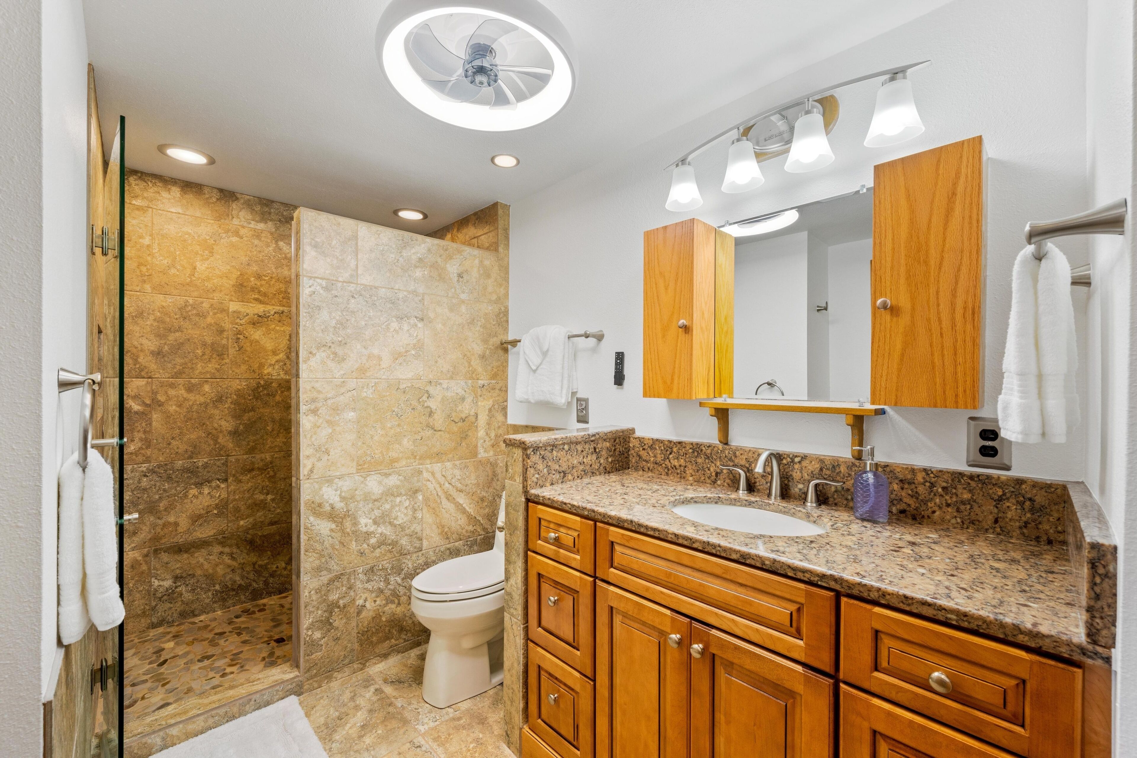 A modern bathroom with a granite countertop, wooden cabinets, a built-in sink, and a glass shower enclosure.