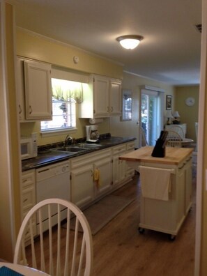 Kitchen with a window offering a view of the outside, featuring a chair, cart, and clock.