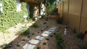 Stroll along the winding garden pathway to a serene seating area surrounded by lush plants and a decorative birdbath.