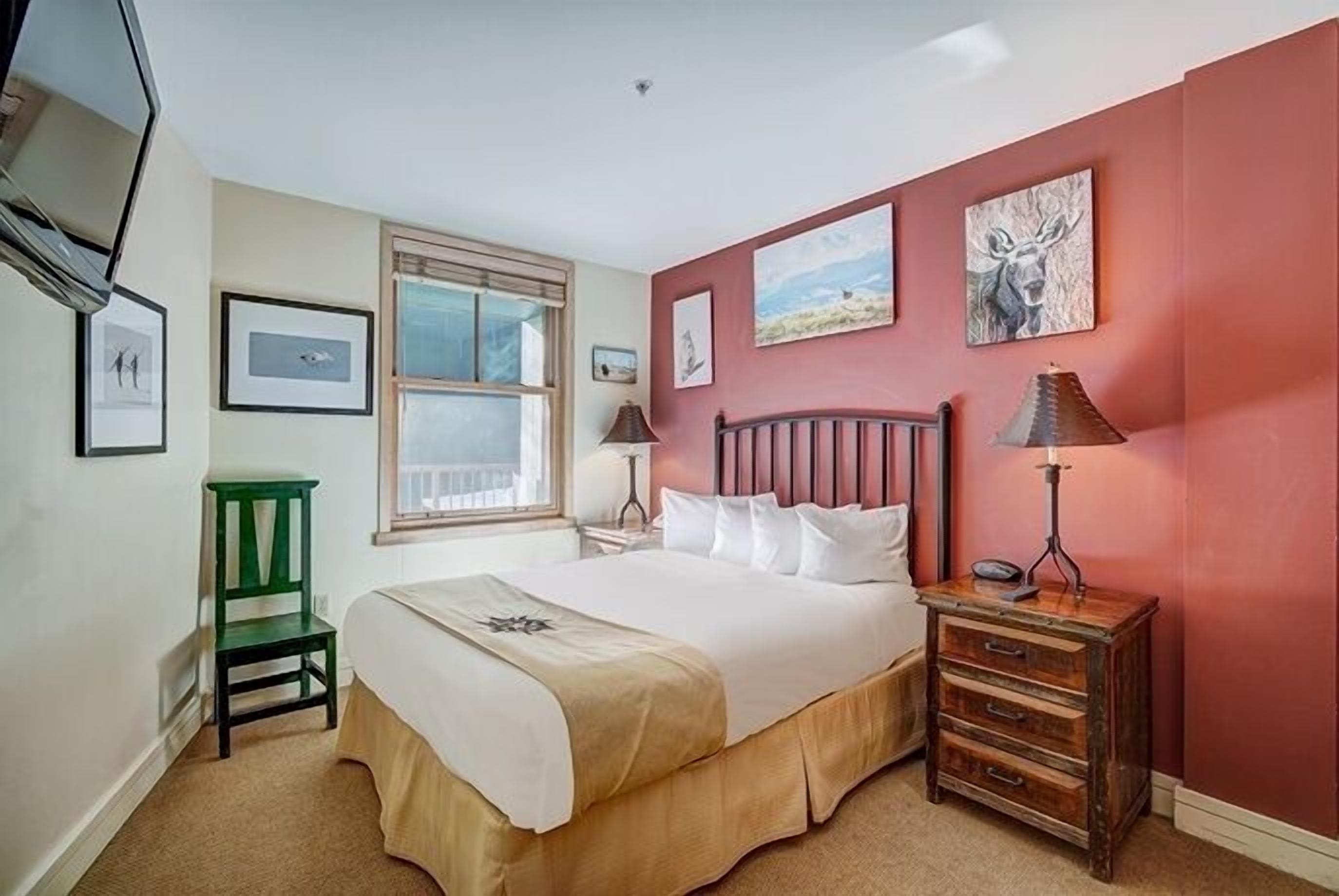 A bedroom with a bed, a green chair, a wooden nightstand, and a lamp.