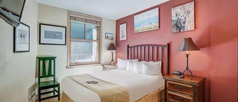 A bedroom with a bed, a green chair, a wooden nightstand, and a lamp.