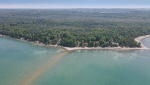 Ein Luftbild einer Küstenlandschaft mit Sandstrand, dichtem Wald und klarem türkisblauem Wasser.
