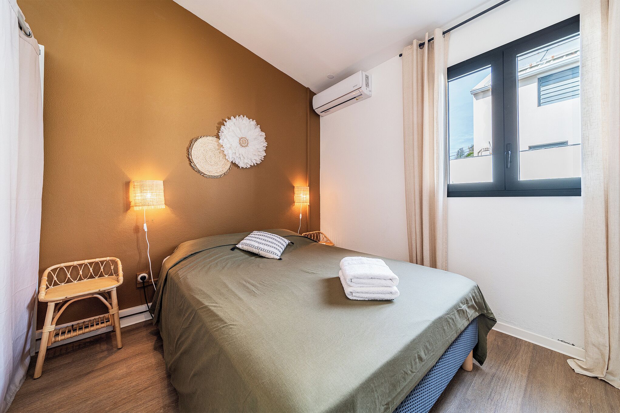 Et soveværelse med en seng, sengeborde med lamper, en stol og en aircondition.
