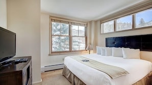 Une chambre d’hôtel avec un grand lit, une télévision et une fenêtre donnant sur des arbres.