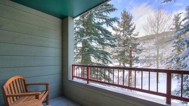 Un balcon en bois offrant une vue sur des arbres couverts de neige et doté d’une rambarde rouge.