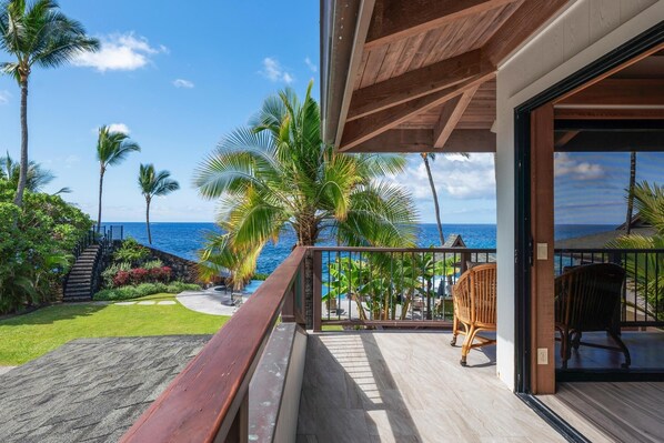 A balcony with a view of the ocean, palm trees, and a wooden deck.