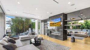 A modern living room with a fireplace, comfortable seating, and a large window offering a view of greenery.