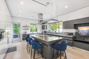 Una cocina moderna con una isla grande, taburetes de bar y un televisor en la pared.