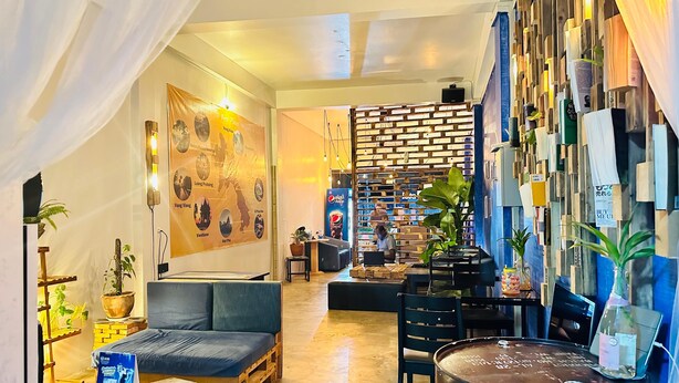 A cozy, modern lounge area with a sofa, a coffee table, and a wooden wall with various items. - TT Hostel (Vientiane)