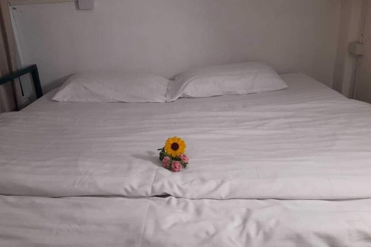 A bed with white linens, a wooden headboard, and a single yellow flower with pink petals on the bed.