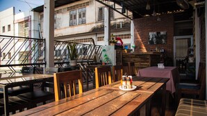 An outdoor dining area with wooden tables and chairs, a brick wall, and a view of buildings in the background. - TT Hostel (Vientiane)