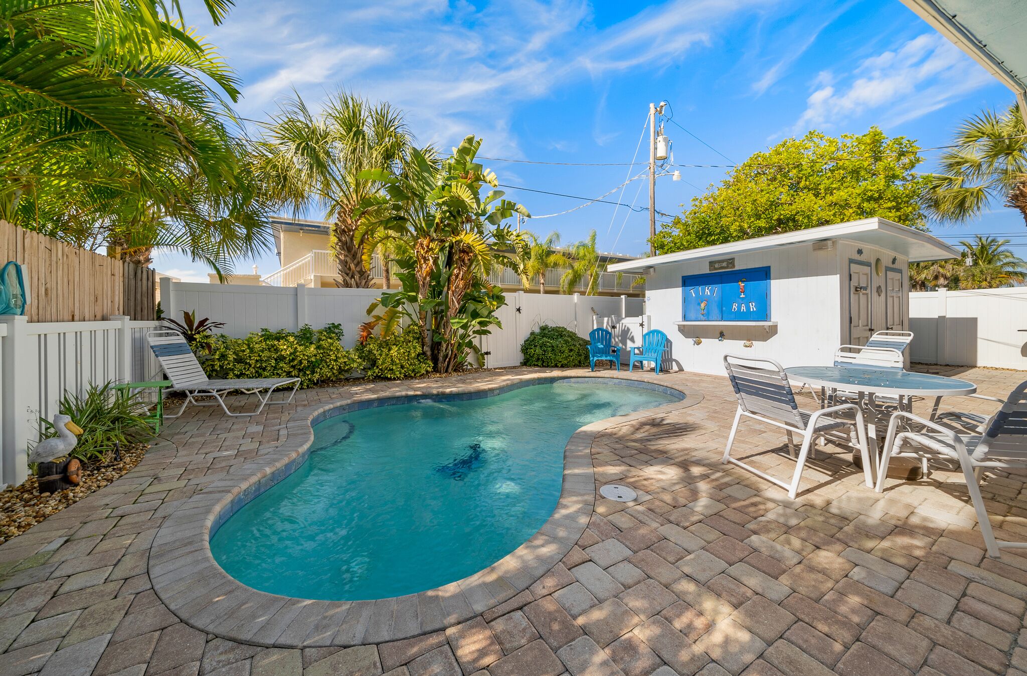 A backyard with a swimming pool, a tiki bar, and outdoor seating.