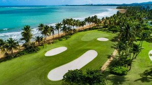 Campo de golf con búnkeres de arena, palmeras y vista al mar.