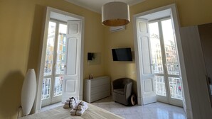 Un dormitorio con cama, cómoda, silla, televisor y balcón con vistas a la ciudad.