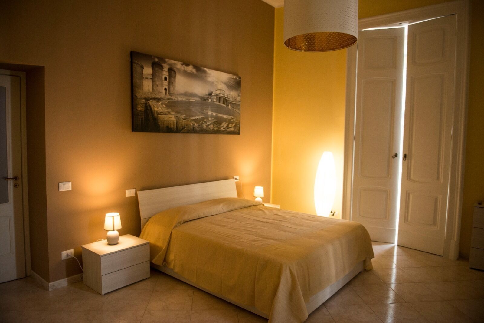 A bedroom with a bed, nightstands, a lamp, a painting, and a door.