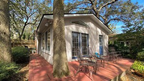 Une petite maison avec un porche, entourée d’arbres et d’une clôture en bois.
