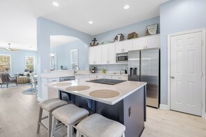 Een moderne keuken met een centraal eiland, witte kasten, roestvrijstalen apparatuur en een eetgedeelte met een ronde tafel en barkrukken.