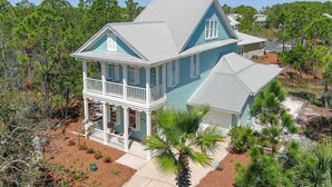 A two-story house with a balcony, surrounded by trees and a sandy area. - Avalon - 3BR/3BA beach house with beach view (Gulf Shores)