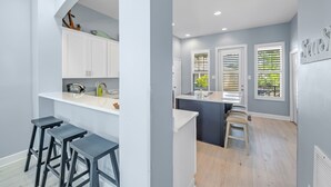 A modern kitchen with white cabinets, a countertop, and bar stools. - Avalon - 3BR/3BA beach house with beach view (Gulf Shores)