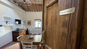 A dining area with a wooden table, white chairs, a chandelier, a television, and a wooden door labeled "Porta del Chiante". - Characteristic apartment in historic 1300s tower (San Casciano in Val di Pesa)