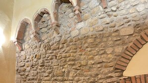 A stone wall with brick accents, a wooden table, and a small stool in a room with tiled flooring. - Characteristic apartment in historic 1300s tower (San Casciano in Val di Pesa)