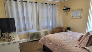 A bedroom with a bed, a chair, a radiator, a television, and a window with curtains. - Huge deck & yard Near Indoor Sports Arena! Spacious! Smart TVs! Fast Wifi! Cozy. (Machesney Park)