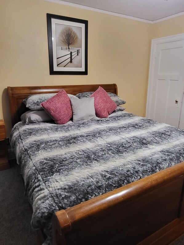 Une chambre avec un lit en bois, un tableau encadré au mur et une porte blanche.