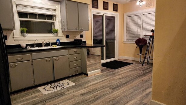 A kitchen with grey cabinets, a black countertop, and a window with blinds. - Huge deck & yard Near Indoor Sports Arena! Spacious! Smart TVs! Fast Wifi! Cozy. (Machesney Park)