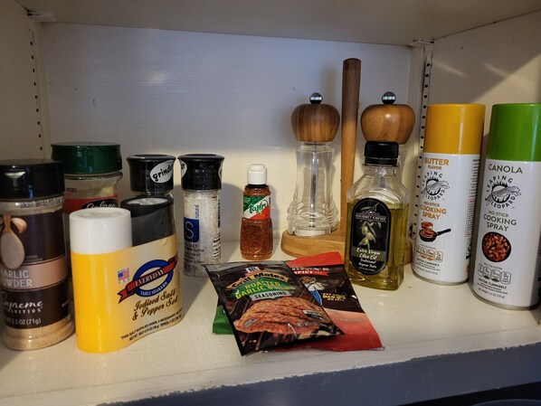 A shelf with various kitchen spices and condiments, including salt, pepper, and cooking sprays.