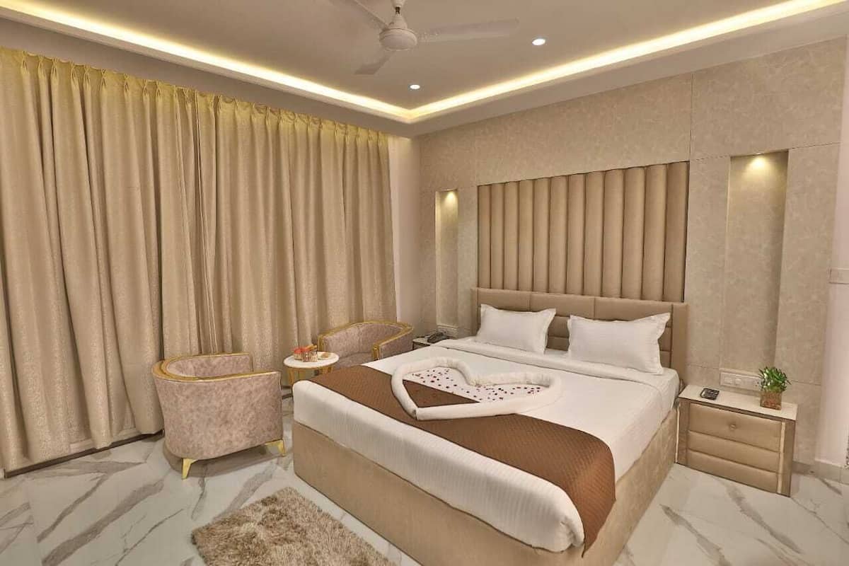 A modern bedroom with a large bed, a headboard, a bedside table, a nightstand, a chair, and a window with curtains.