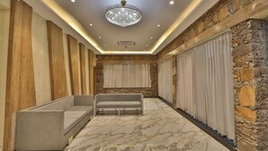Um corredor com parede de pedra, um candelabro, um sofá e uma janela com cortinas.