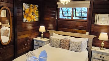 A wooden-paneled room with a bed, two bedside tables, a chandelier, a window, and a wall-mounted thermostat.
