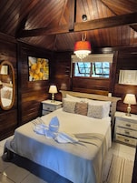 Habitación con paneles de madera, una cama, dos mesitas de noche, un candelabro, una ventana y un termostato instalado en la pared.