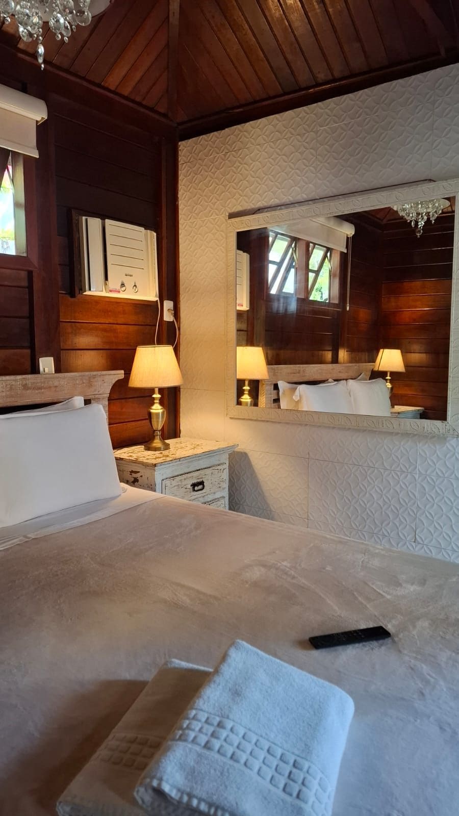 Habitación de hotel con una cama grande, lámparas de noche, un espejo y techo de madera.