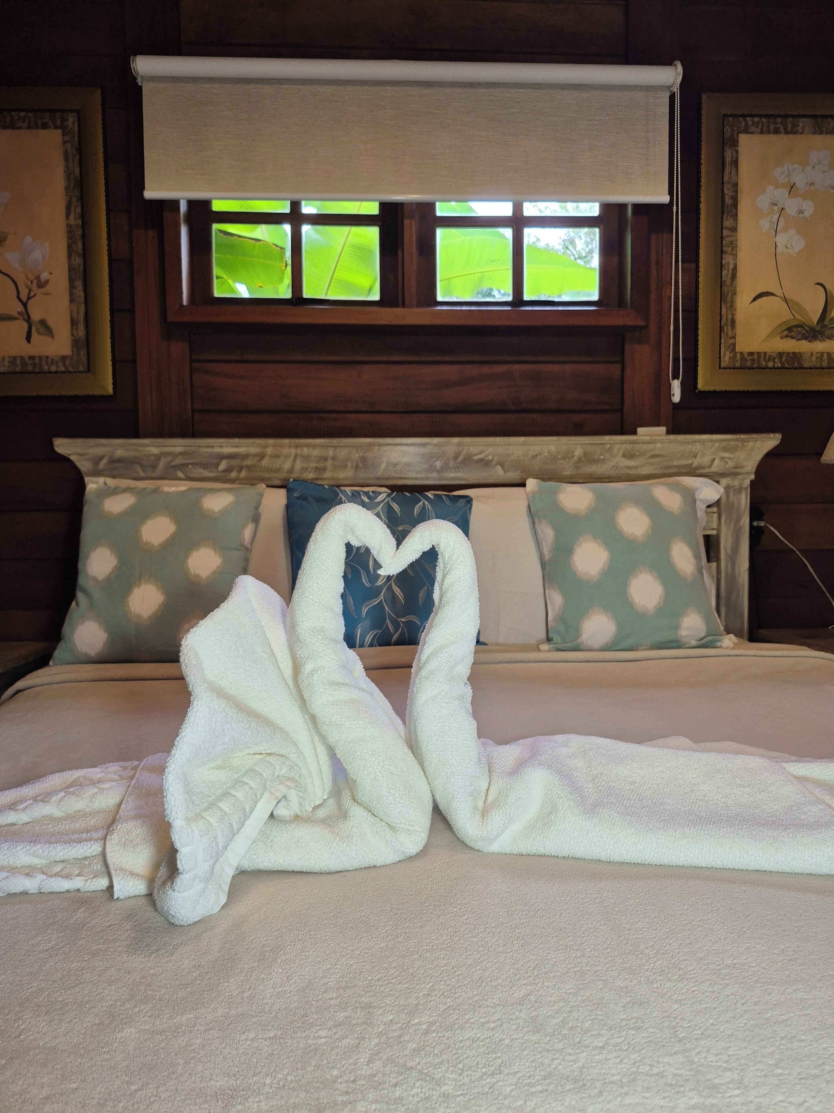 A hotel room with a bed, a window with blinds, and a painting on the wall.