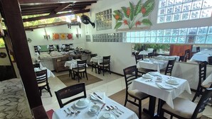 A restaurant with wooden beams, tiled walls, and large windows. Tables are set with white tablecloths and silverware. - Aratinga inn (Angra dos Reis)