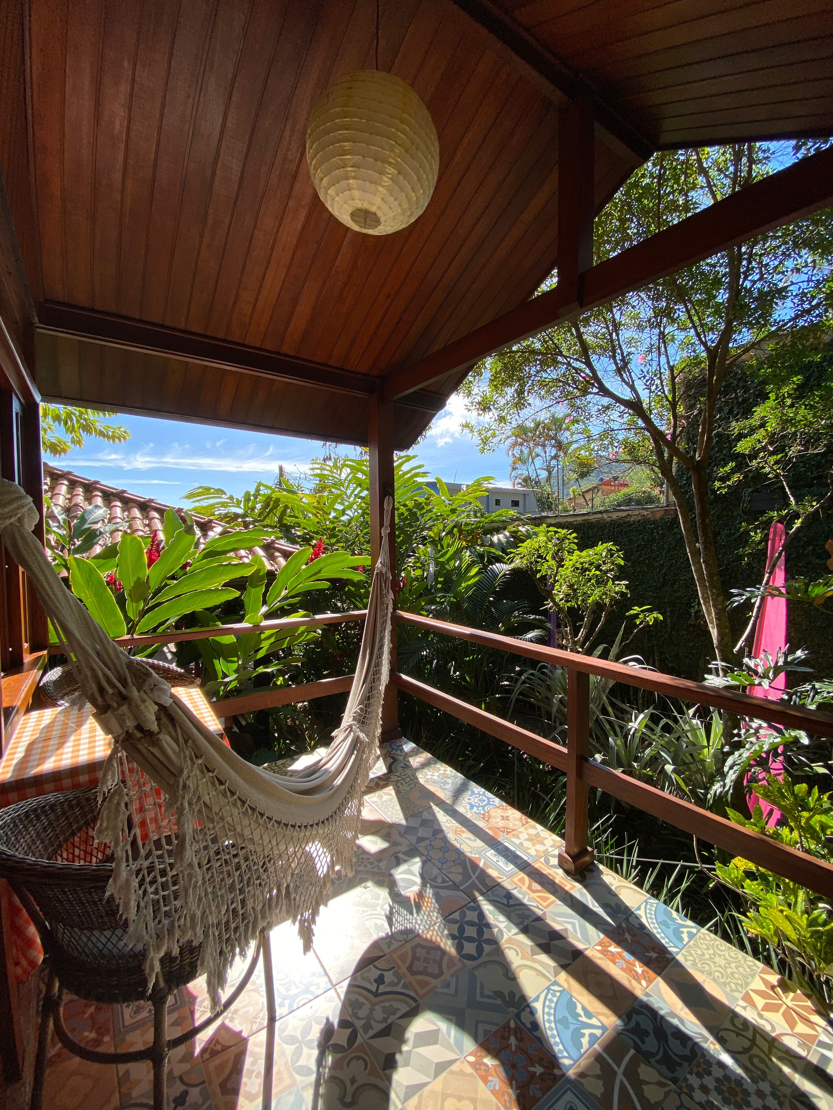 A hammock under a wooden ceiling with a view of lush greenery and a tiled floor.