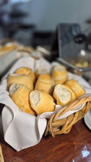 A basket of bread rolls on a wooden table. - Aratinga inn (Angra dos Reis)